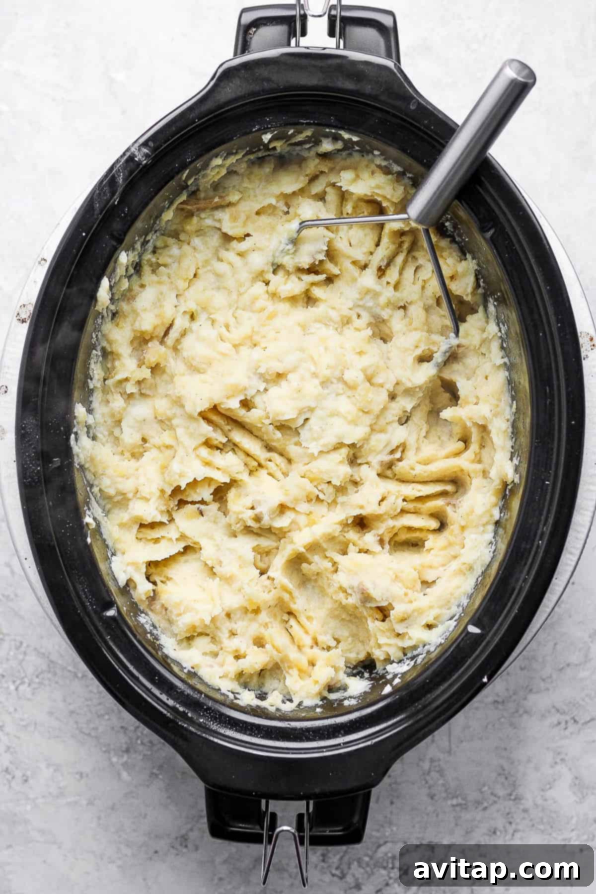 A large pot of creamy mashed potatoes in a slow cooker, garnished with fresh herbs, ready for serving.