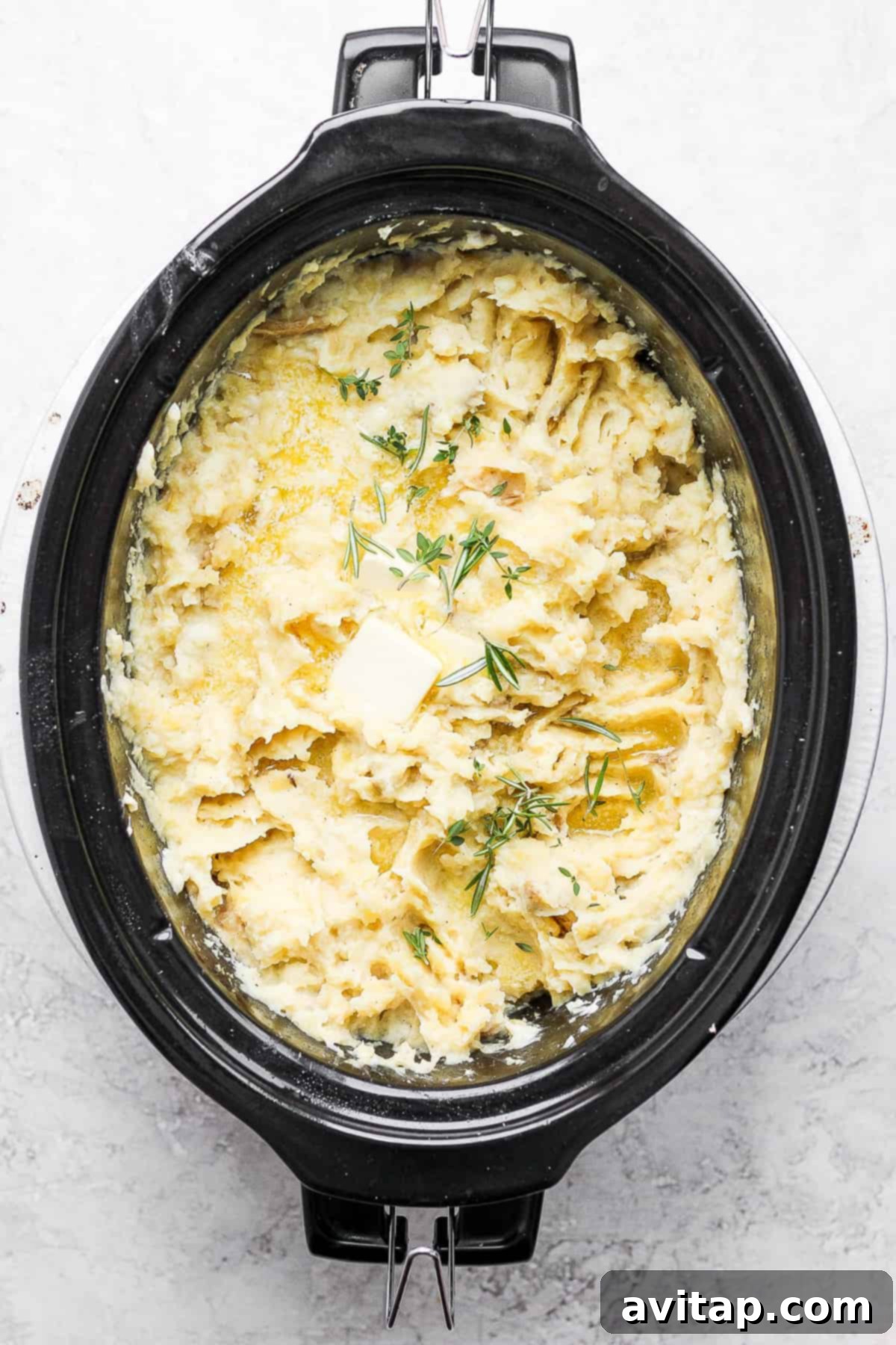 A close-up of beautifully mashed potatoes, garnished with fresh dill, in a slow cooker.