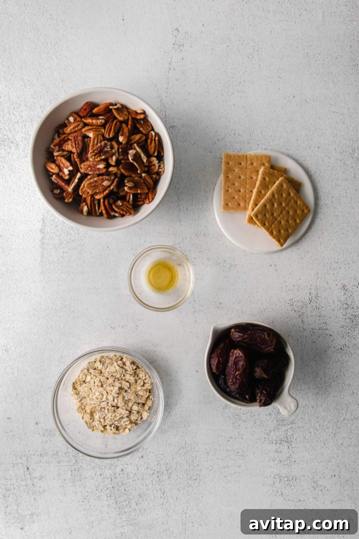A flat lay of ingredients for pecan pie energy balls: whole pecans, graham crackers, a bottle of vanilla extract, pitted dates, and rolled oats in individual bowls.