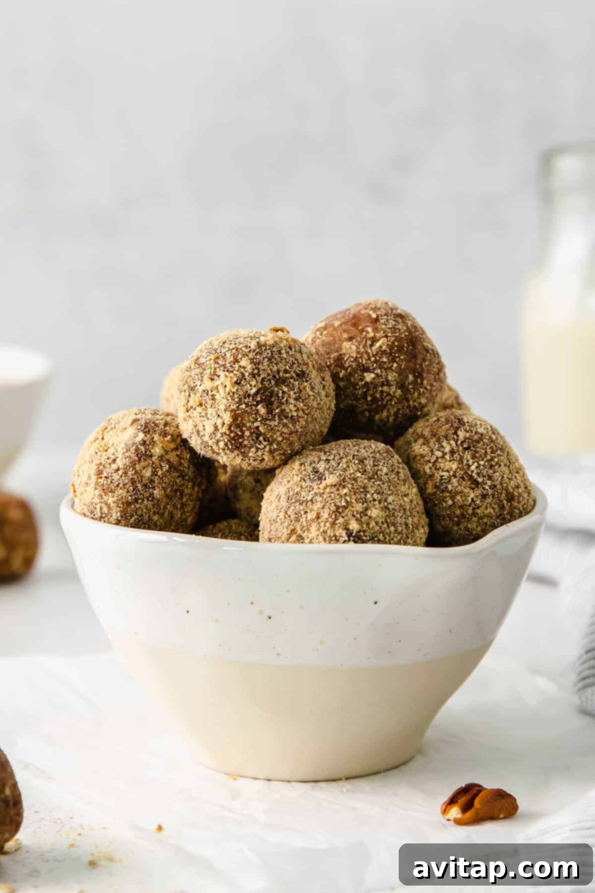 A clear glass bowl brimming with pecan pie energy balls, garnished with a few whole pecans.