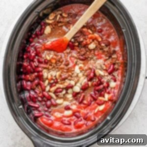 Slow cooker chili with beans, stirred with a wooden spoon.