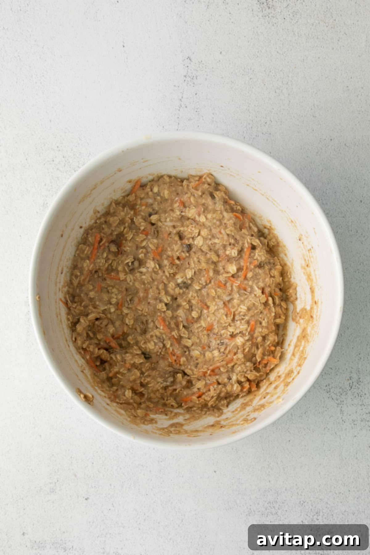 Morning Glory Baked Oatmeal Batter The smooth, thick batter of Morning Glory Baked Oatmeal, studded with vibrant orange carrots and golden raisins, sitting in a mixing bowl before baking.