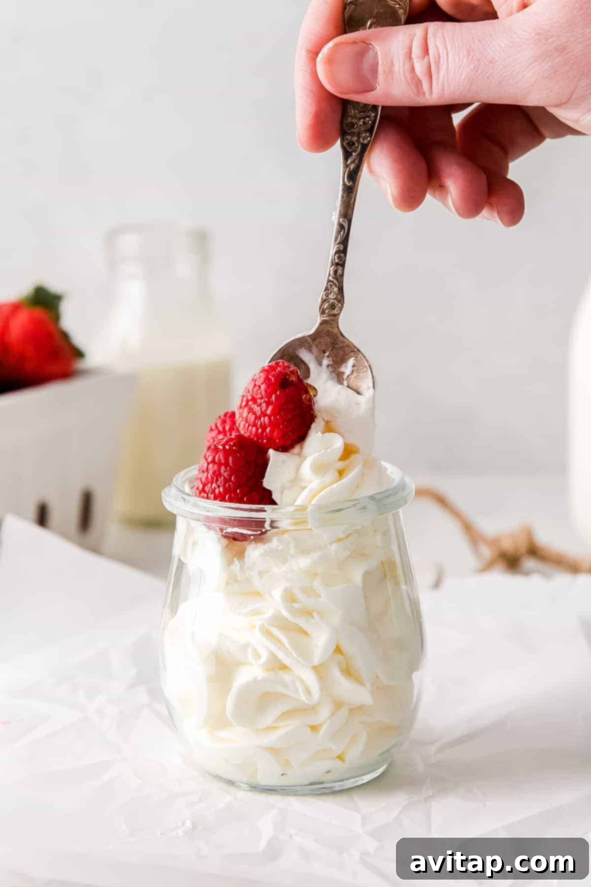 Perfect Homemade Whipped Cream 7 A spoonful of fluffy homemade whipped cream topped with vibrant, fresh raspberries, ready to be enjoyed.