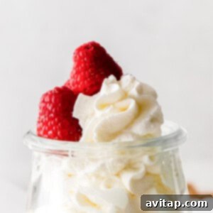 Perfect Homemade Whipped Cream 8 A glass container filled with whipped cream, topped with two fresh raspberries, ready to be served.