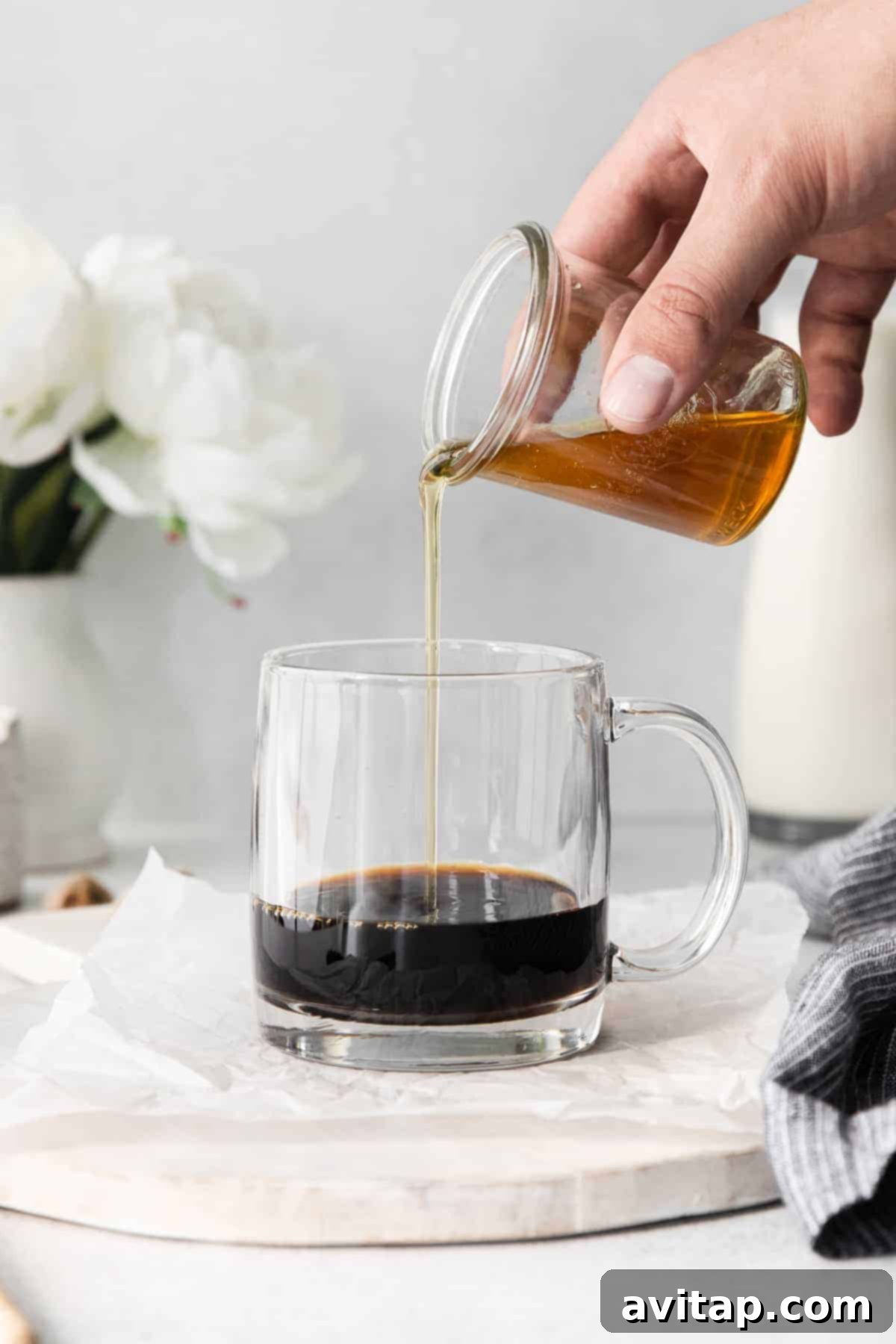 A stream of golden honey simple syrup being poured into freshly brewed espresso in a clear glass, illustrating the initial step in crafting a miel latte.