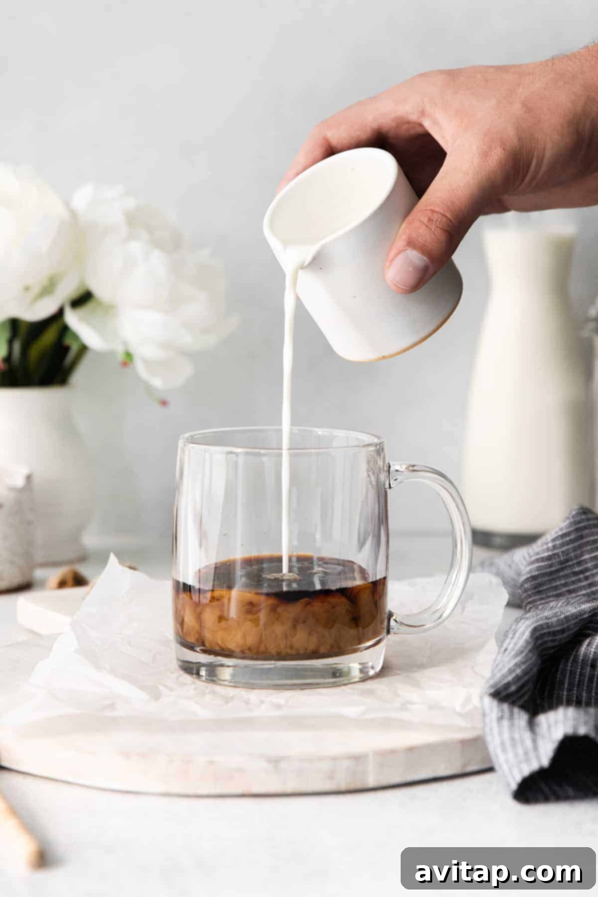 Creamy frothed milk being gently poured into a coffee mug containing espresso, creating distinct layers for a miel latte.