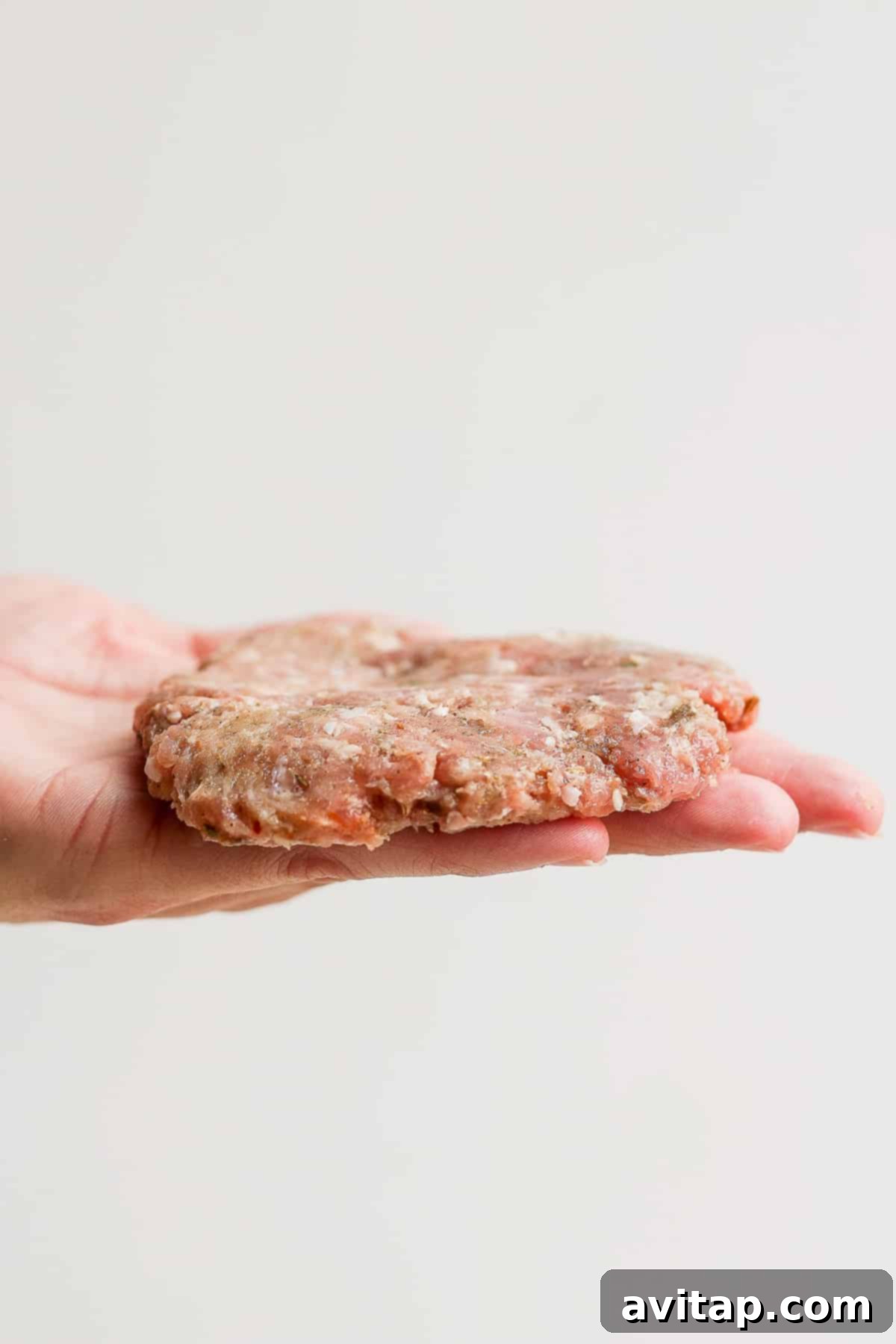 A perfectly formed, thin breakfast sausage patty resting in the palm of a hand, showcasing its ideal size and thickness.