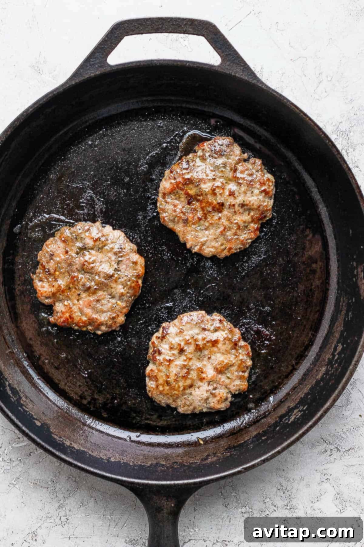 Two breakfast sausage patties sizzling and browning perfectly in a cast iron skillet on the stovetop.