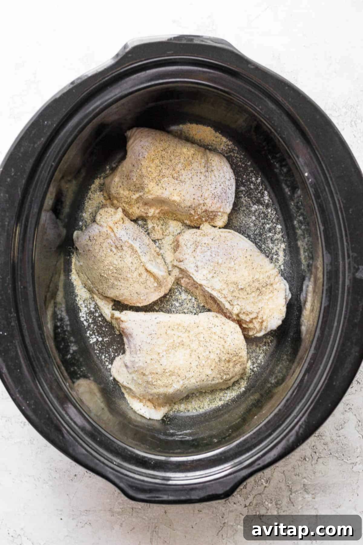 Seasoned chicken thighs cooking inside a slow cooker with aromatic vegetables and broth.