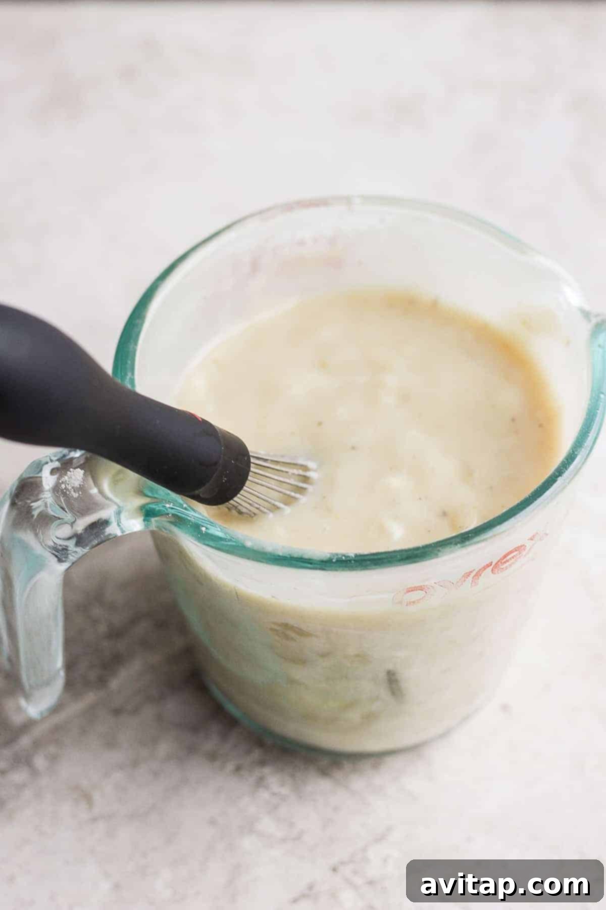 A smooth, thick flour slurry being added to a slow cooker to thicken the chicken and dumpling broth.