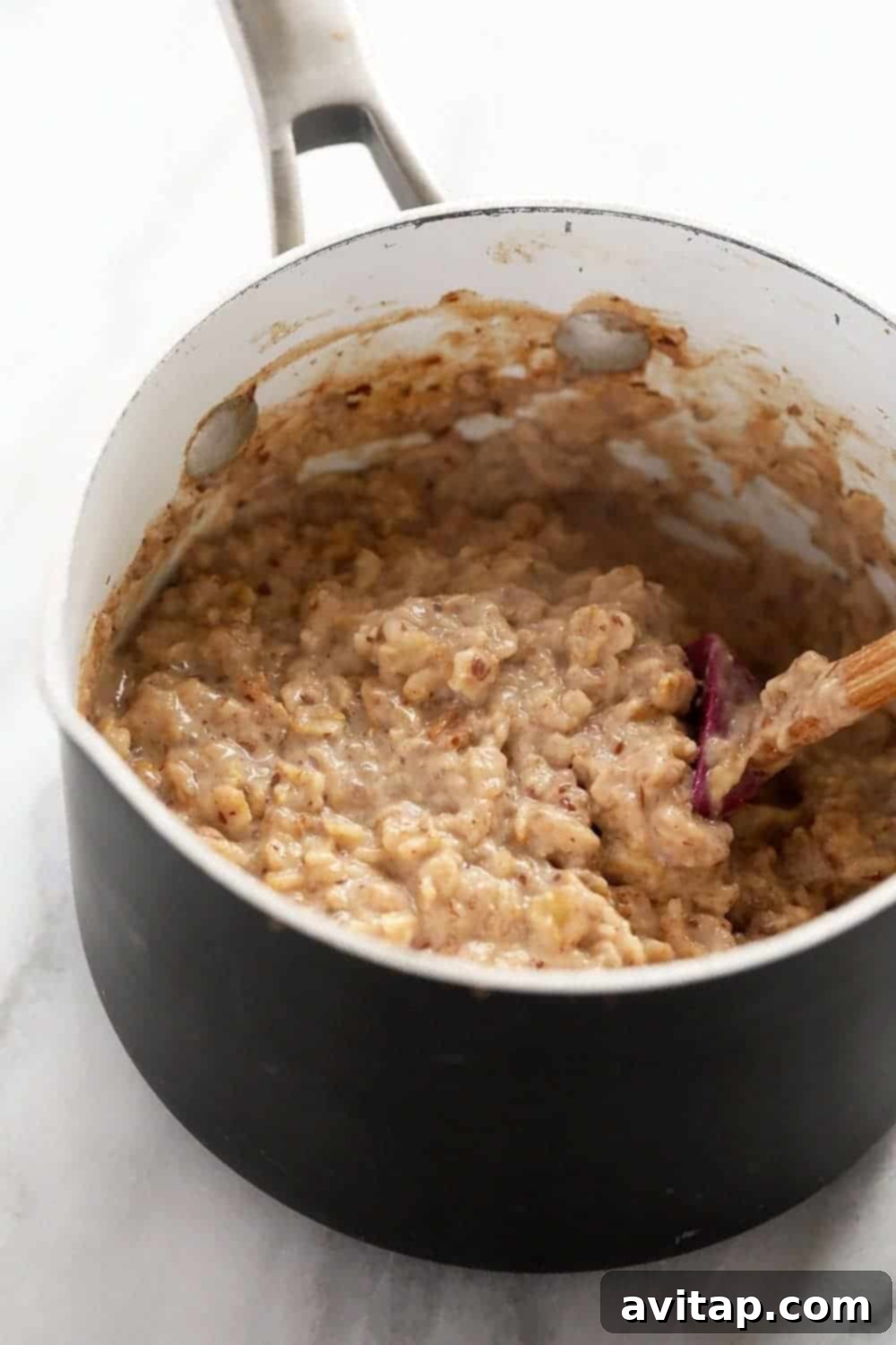 Close-up shot of creamy oatmeal being stirred with a wooden spoon in a saucepan, showcasing its perfect, smooth texture.