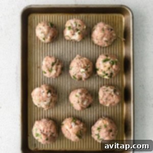 Neatly formed golf-ball sized turkey meatballs arranged on a baking sheet, ready for cooking