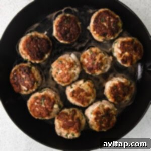 Partially browned turkey meatballs sizzling in a skillet with olive oil