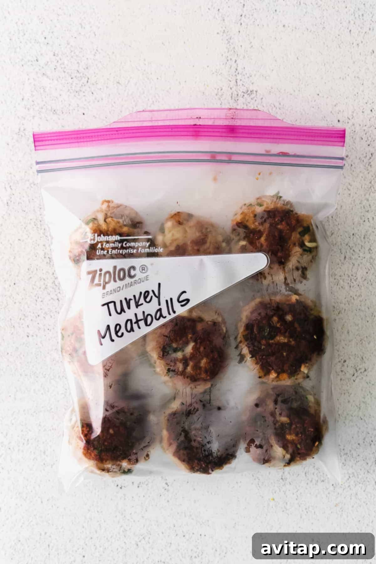 A close-up shot of a single perfectly cooked, golden-brown ground turkey meatball on a light background, highlighting its tender texture