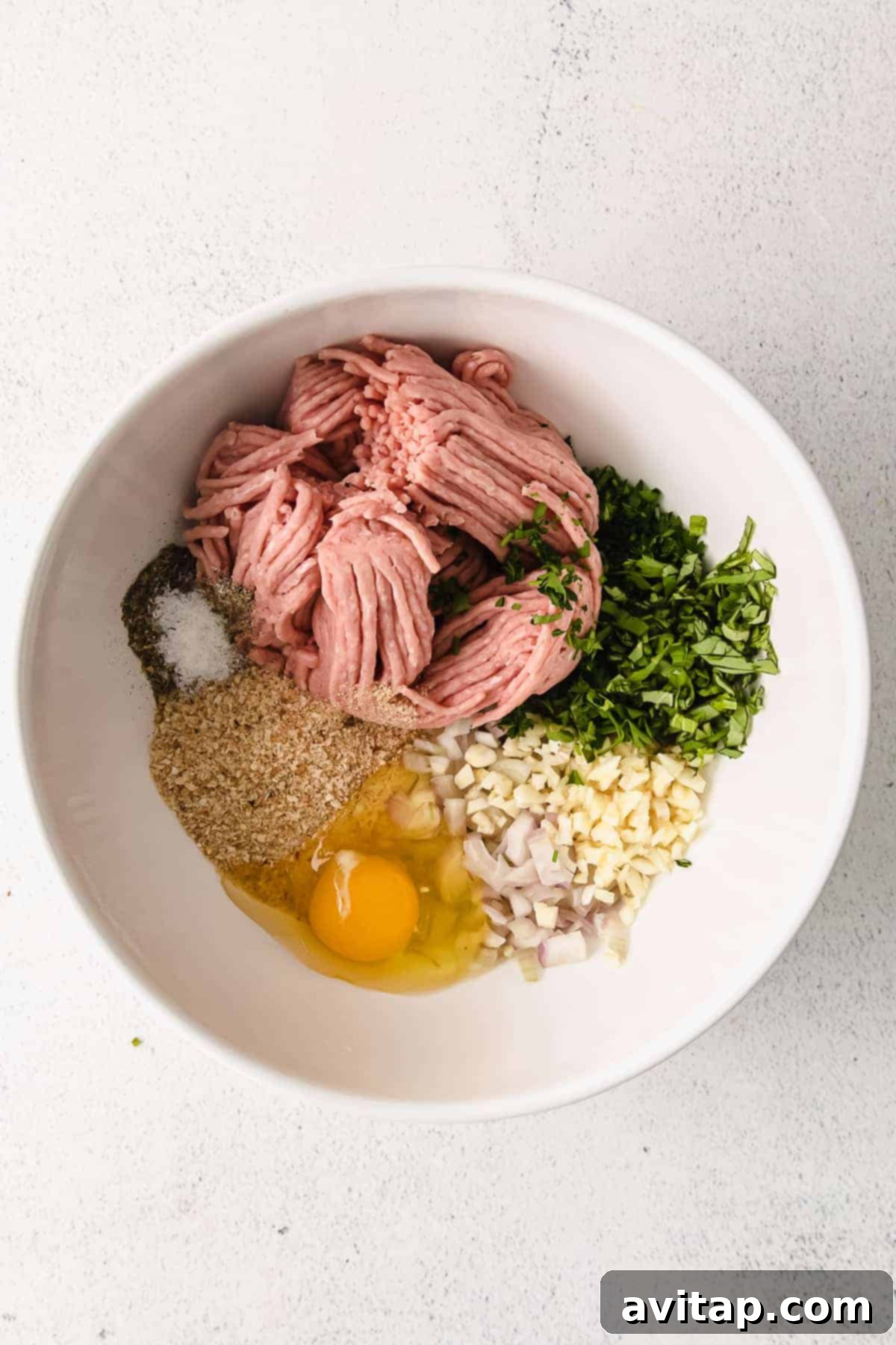 A vibrant flat lay of all fresh and dried ingredients for turkey meatballs, including ground turkey, herbs, shallots, garlic, and butter