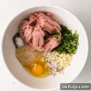 All ingredients for turkey meatballs, including ground turkey, egg, breadcrumbs, and herbs, combined in a large white bowl