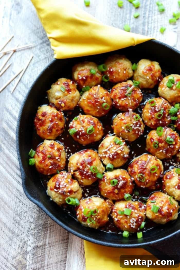Healthy Baked Chicken Meatballs coated in sauce, garnished with sesame seeds.
