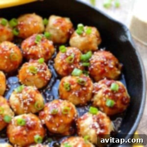 A skillet filled with cooked Kung Pao Chicken Meatballs garnished with sesame seeds and chopped green onions.
