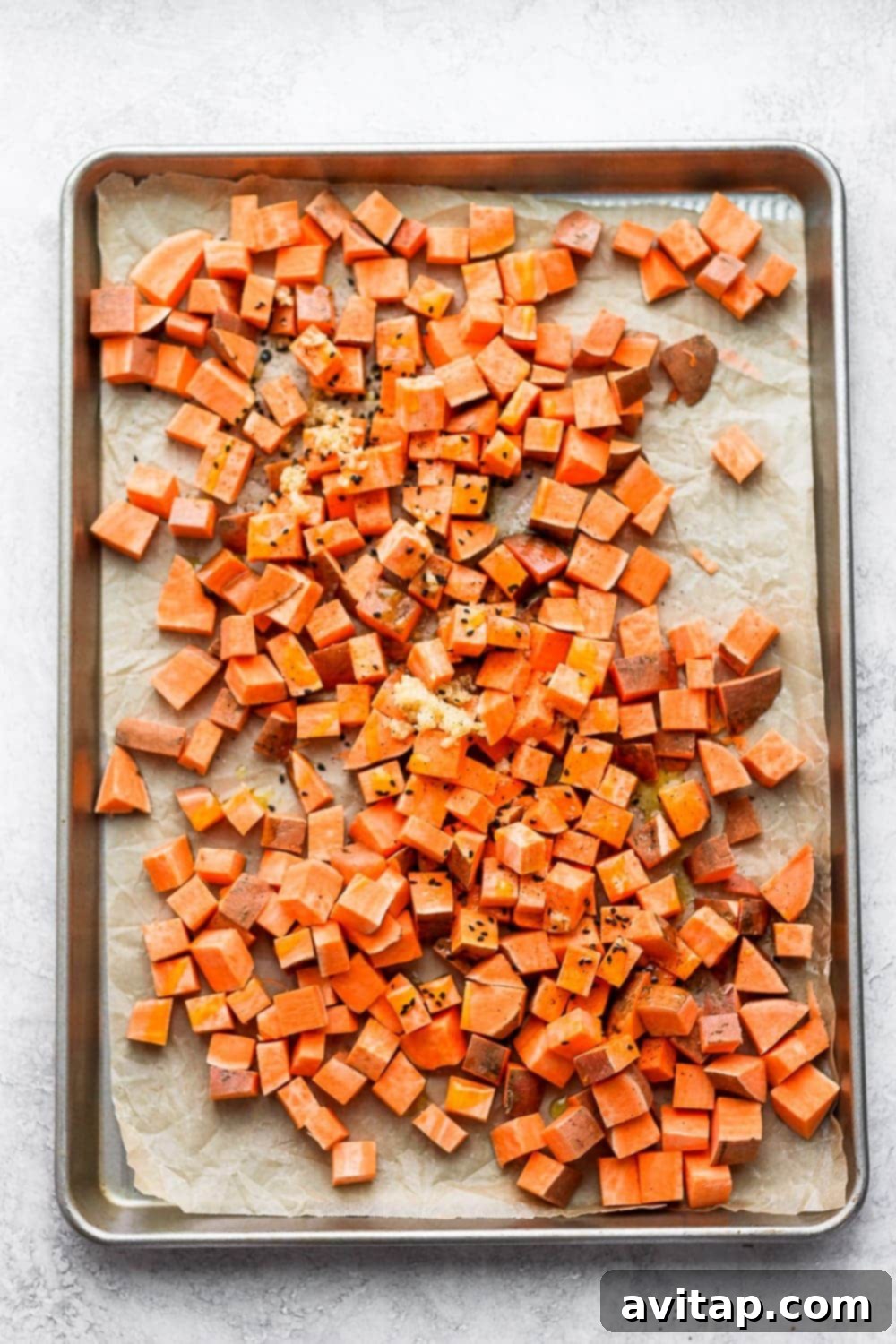 Close-up of perfectly roasted sweet potato cubes on a baking sheet, seasoned with black sesame seeds.