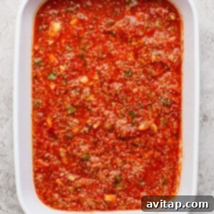Close-up of a white baking dish filled with red tomato sauce mixed with visible herbs and spices.