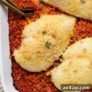 Baked chicken breasts with cheese on a bed of tomato sauce, garnished with parsley and grated cheese, in a white dish.