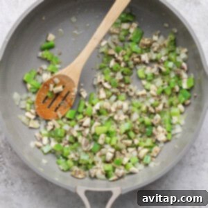 A pan with diced green bell pepper, onion, and mushroom being sautéed with a wooden spoon.