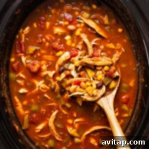 Shredded chicken being returned to a slow cooker filled with chicken enchilada soup, with a wooden spoon for stirring.