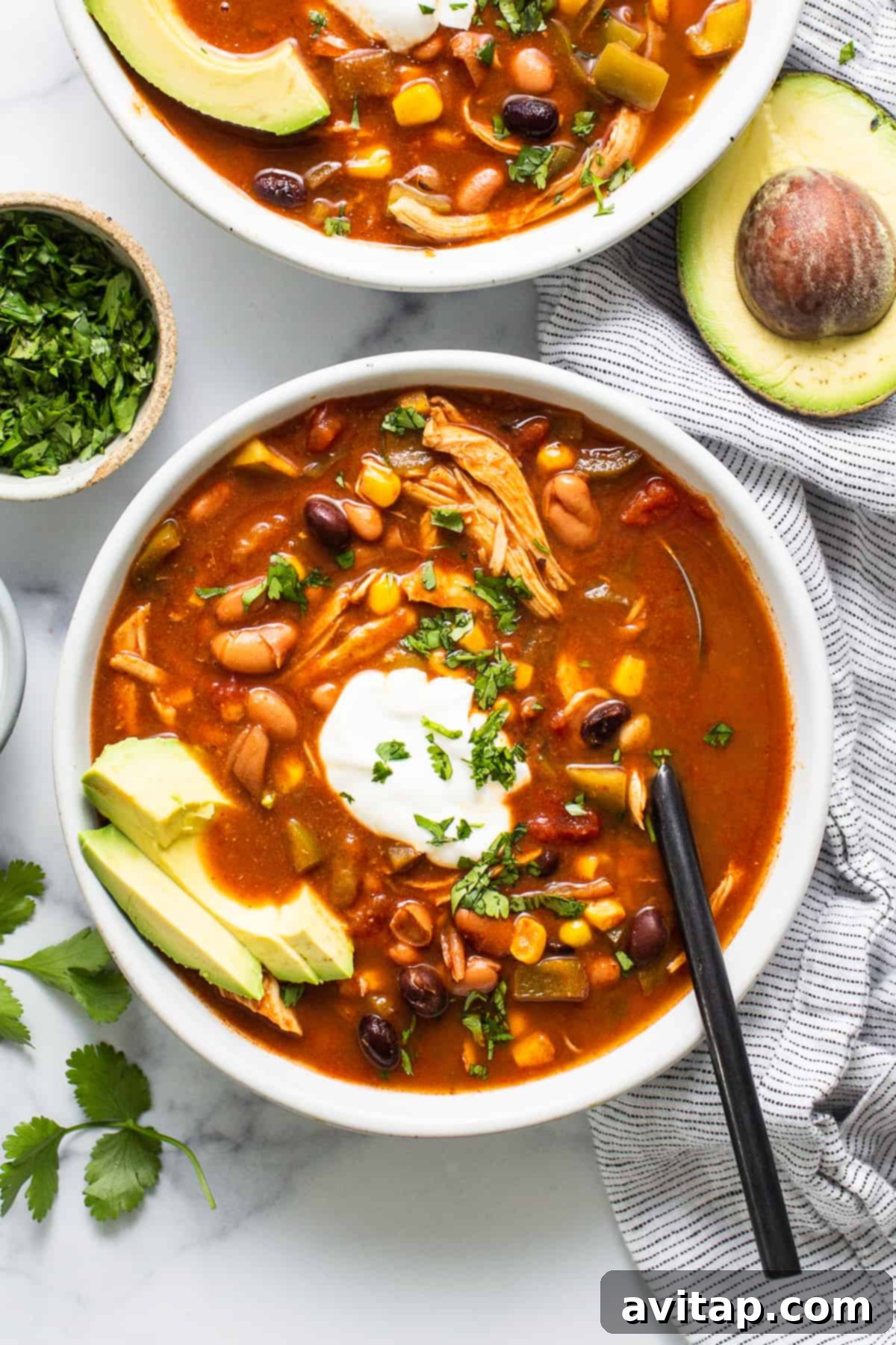 A vibrant bowl of crockpot chicken enchilada soup garnished generously with fresh cilantro, creamy avocado slices, and a swirl of Greek yogurt, showcasing the rich colors and inviting texture of the dish, ready for enjoyment.