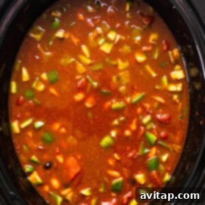 A slow cooker filled with chicken enchilada soup ingredients simmering, with corn added and stirred in.