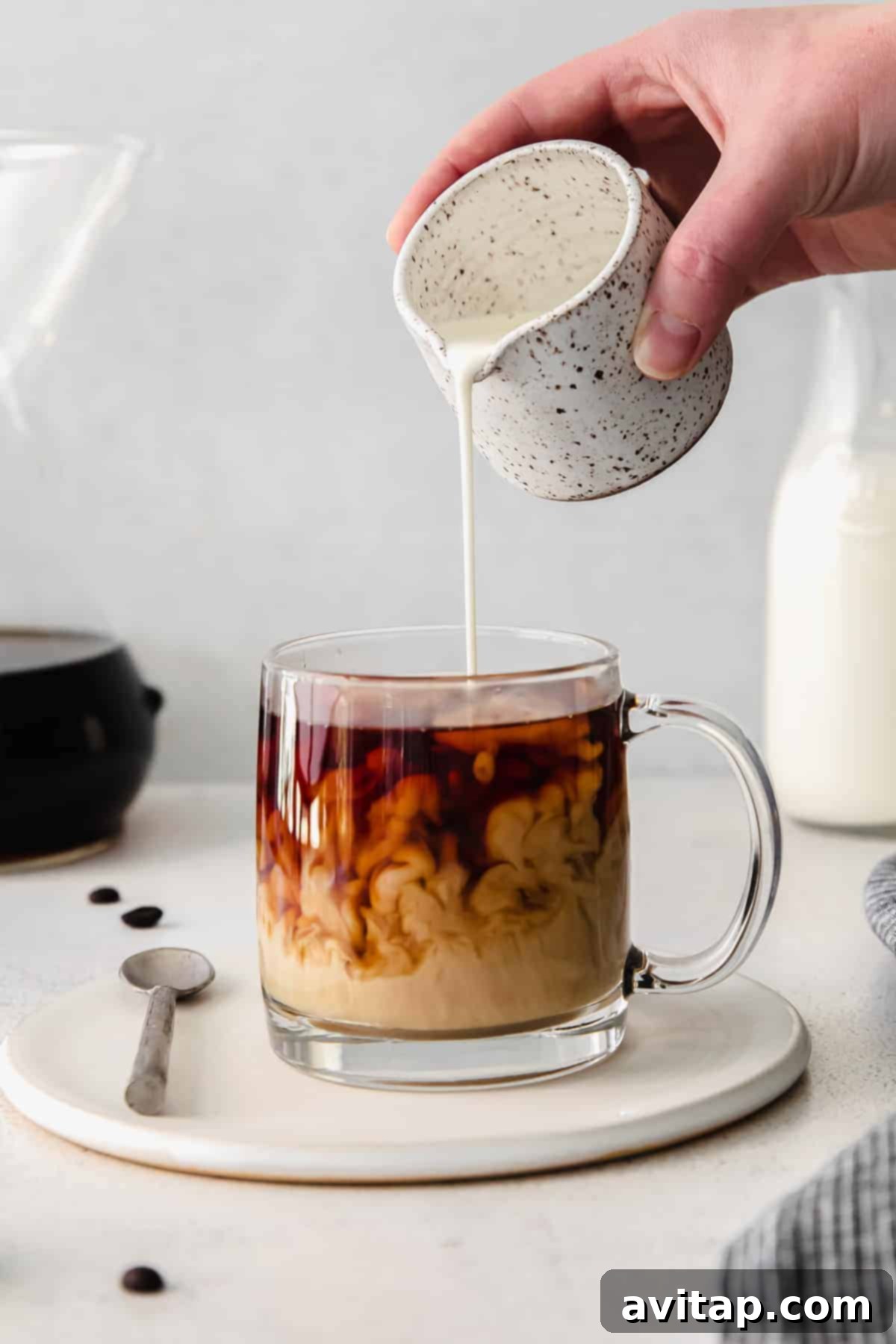 A stream of cream being poured into a mug of pour-over coffee, creating a beautiful swirl.
