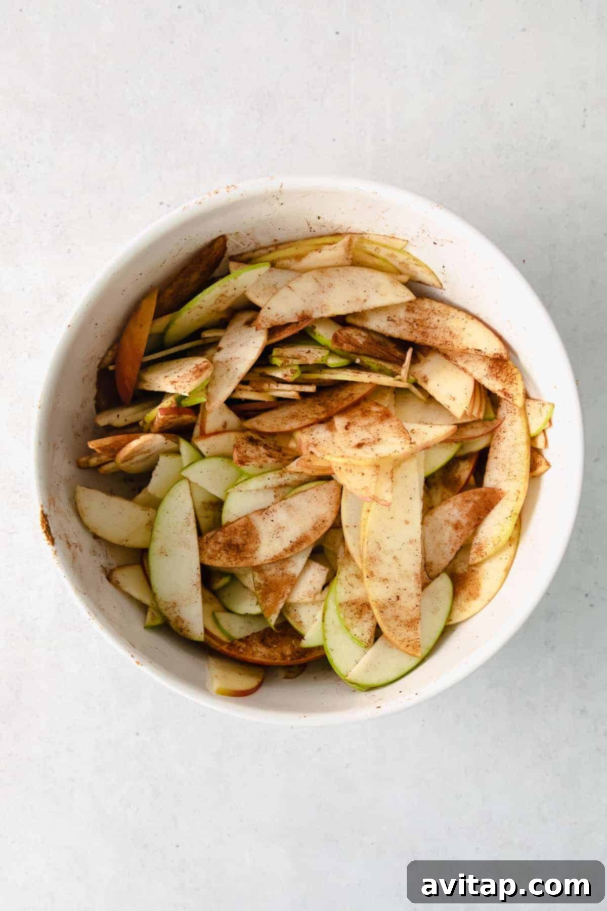 Golden Apple Tart 4 Thinly sliced apples tossed with a blend of warm spices and brown sugar in a mixing bowl, ready for the tart.