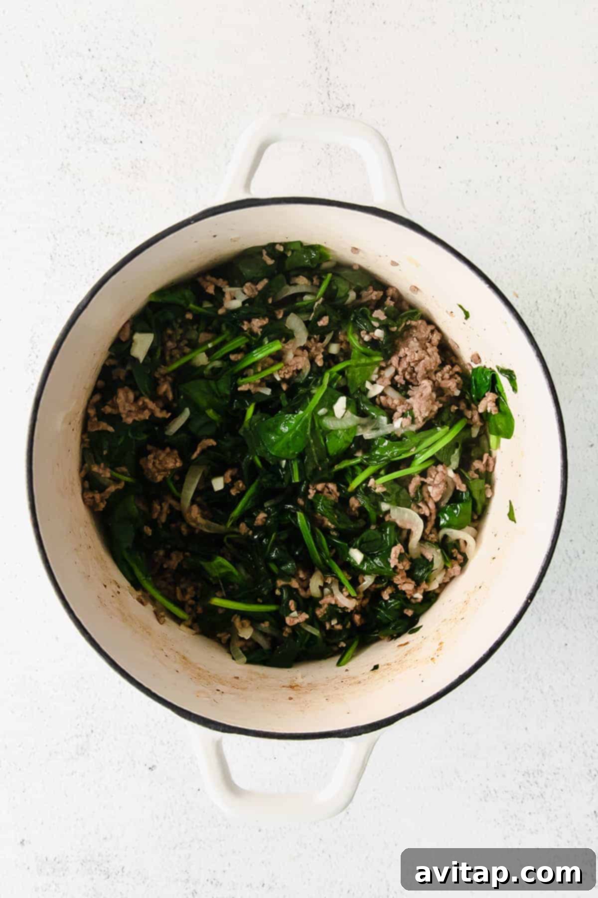 Savory ground meat, vibrant spinach, and aromatic onions simmering together in a large Dutch oven, creating a hearty and fragrant base for the creamy lasagna roll-up filling. Steam gently rises from the pot.