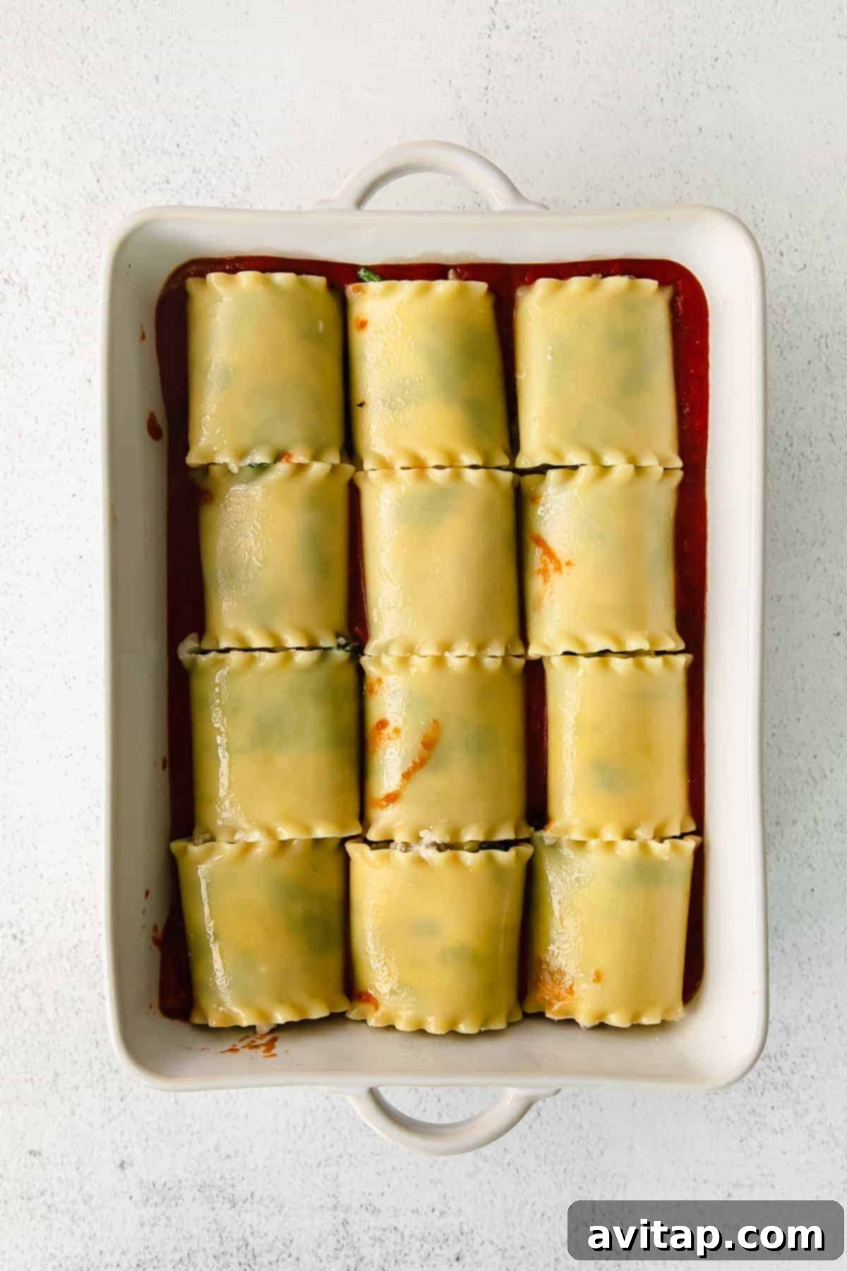 A rectangular casserole dish filled with rows of perfectly baked lasagna roll ups, their tops golden and bubbling with melted mozzarella and parmesan cheese, swimming in a rich marinara sauce, fresh from the oven.