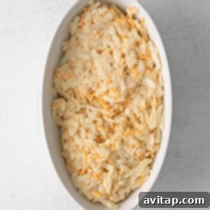 Shredded hash browns mixed with cheese sauce in a white dish, ready for baking.