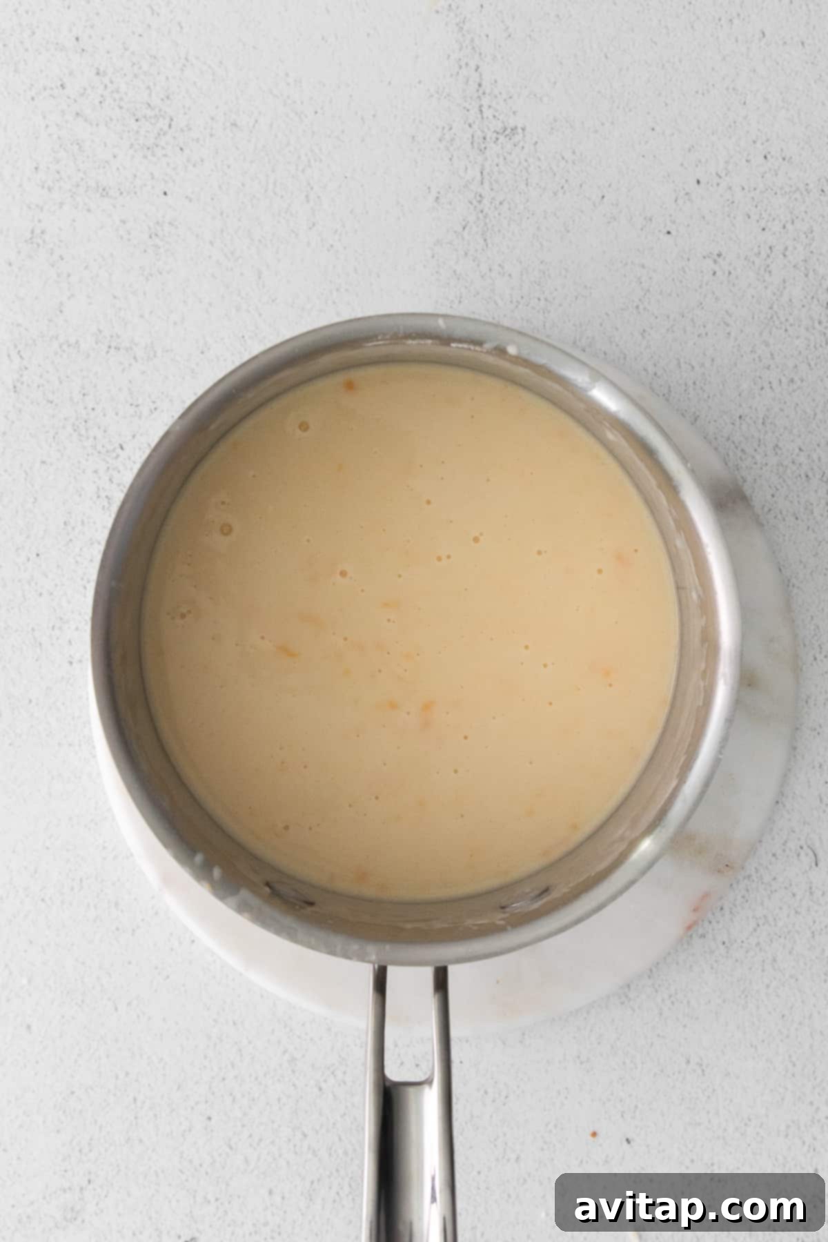 Thick, creamy cheese sauce, made from a roux, simmering in a saucepan, ready to be mixed into the hash browns for the ultimate casserole.