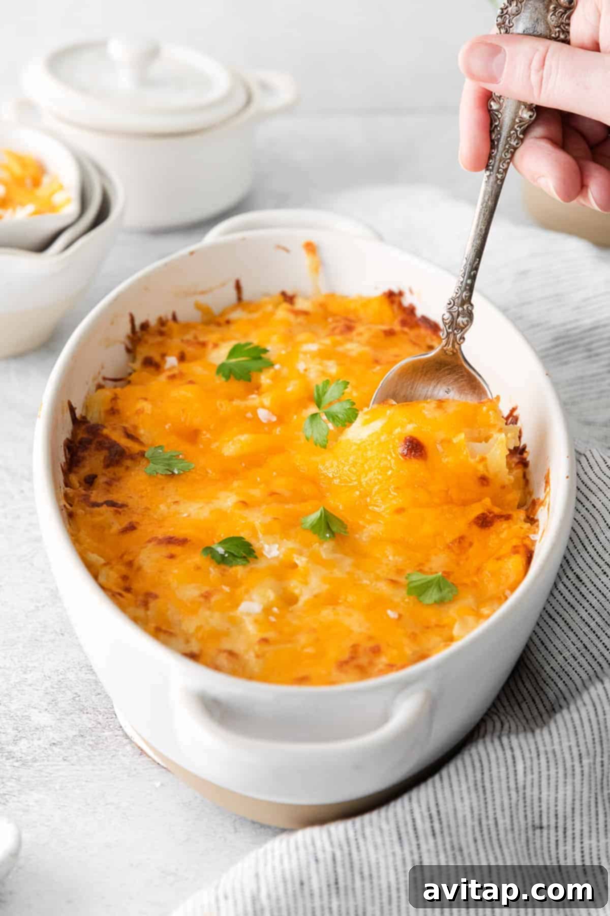Hash browns coated in a creamy cheese sauce, spread evenly in a casserole dish before baking, showcasing the preparation stage.