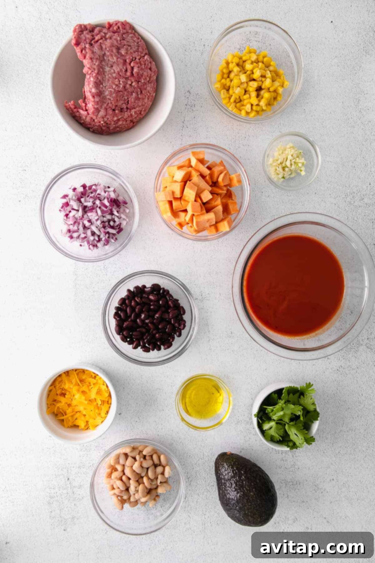 A vibrant selection of ingredients for enchilada skillet laid out in small bowls, including diced sweet potatoes, minced red onion, corn, beans, and ground turkey.
