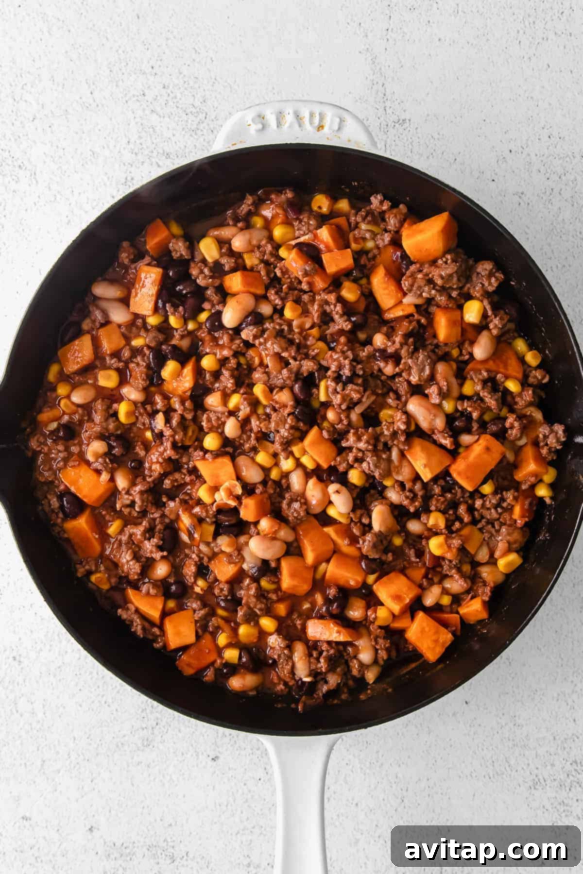 The savory ingredients of the turkey sweet potato enchilada skillet simmering together in a cast iron skillet, before cheese is added.