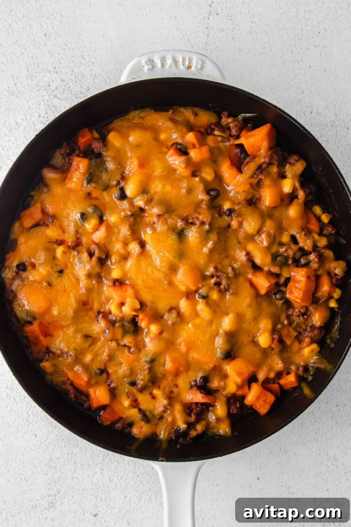 Close-up of the turkey sweet potato enchilada skillet, generously topped with perfectly melted shredded cheese and ready for garnish.