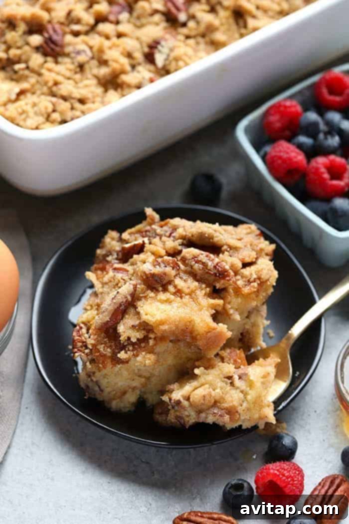 A slice of Maple Pecan Sourdough Overnight French Toast Bake on a plate, garnished with fresh berries and a drizzle of syrup, showcasing its golden-brown perfection.