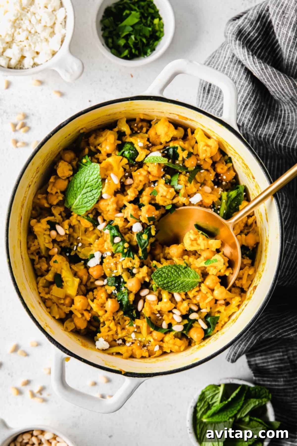 A vibrant bowl of one-pot yellow rice with perfectly marinated chickpeas, cauliflower, and spinach, garnished with fresh herbs.
