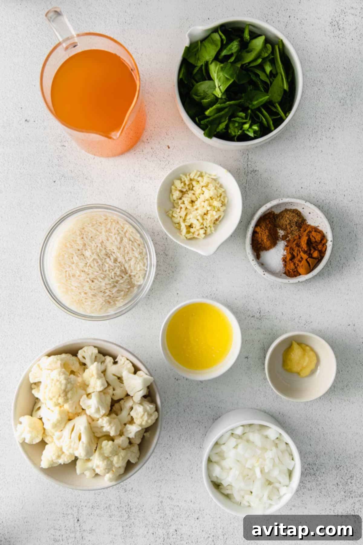 Assorted key ingredients for one-pot yellow rice, including spices, basmati rice, chickpeas, cauliflower, and spinach, neatly arranged in small bowls.
