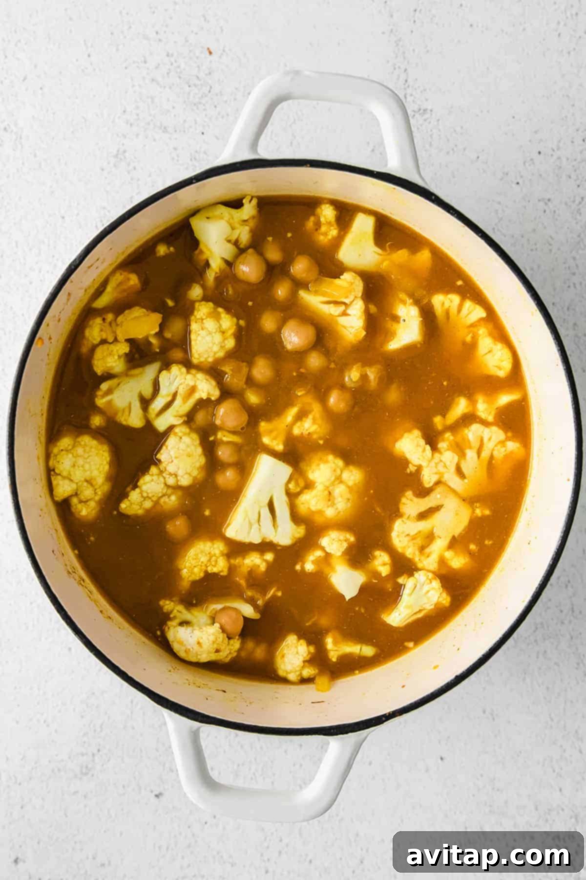 All the vibrant ingredients for the yellow rice recipe, including seasoned chickpeas, cauliflower, and rice, layered inside a Dutch oven before cooking.
