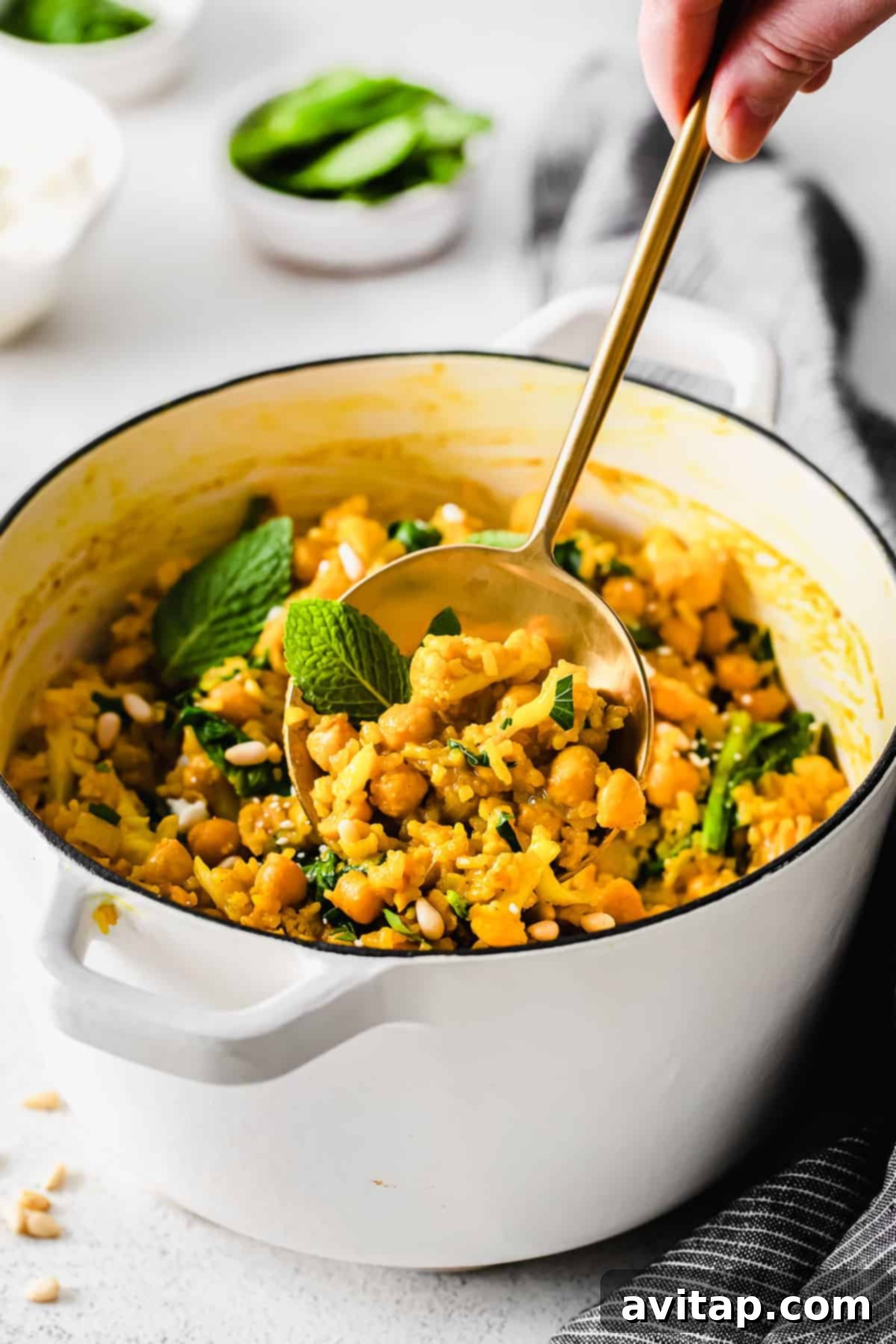 A spoon lifting a generous portion of flavorful yellow rice, garnished with fresh herbs and pine nuts.