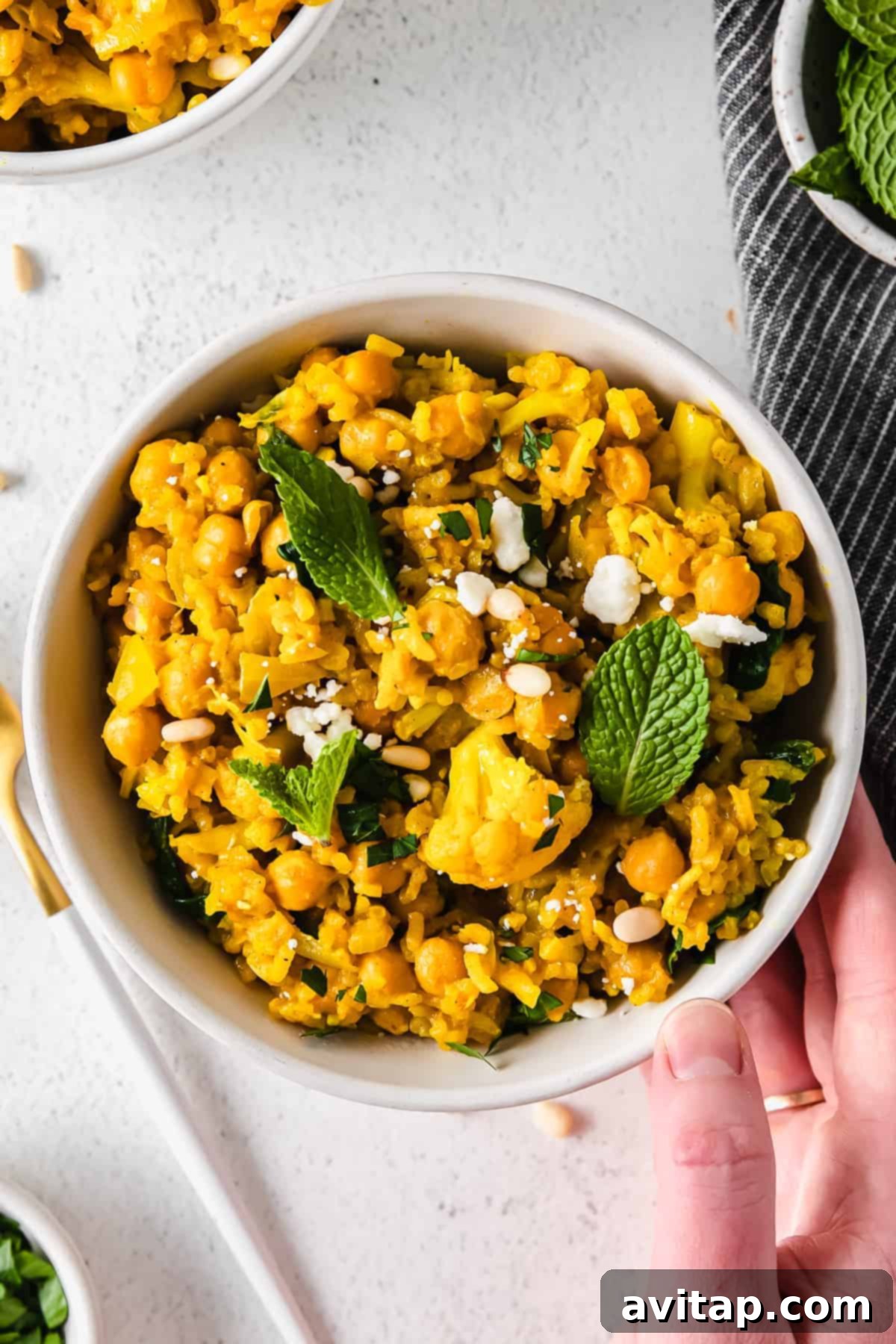 A beautifully presented bowl of one-pot yellow rice, topped with fresh herbs and a sprinkle of feta crumbles.