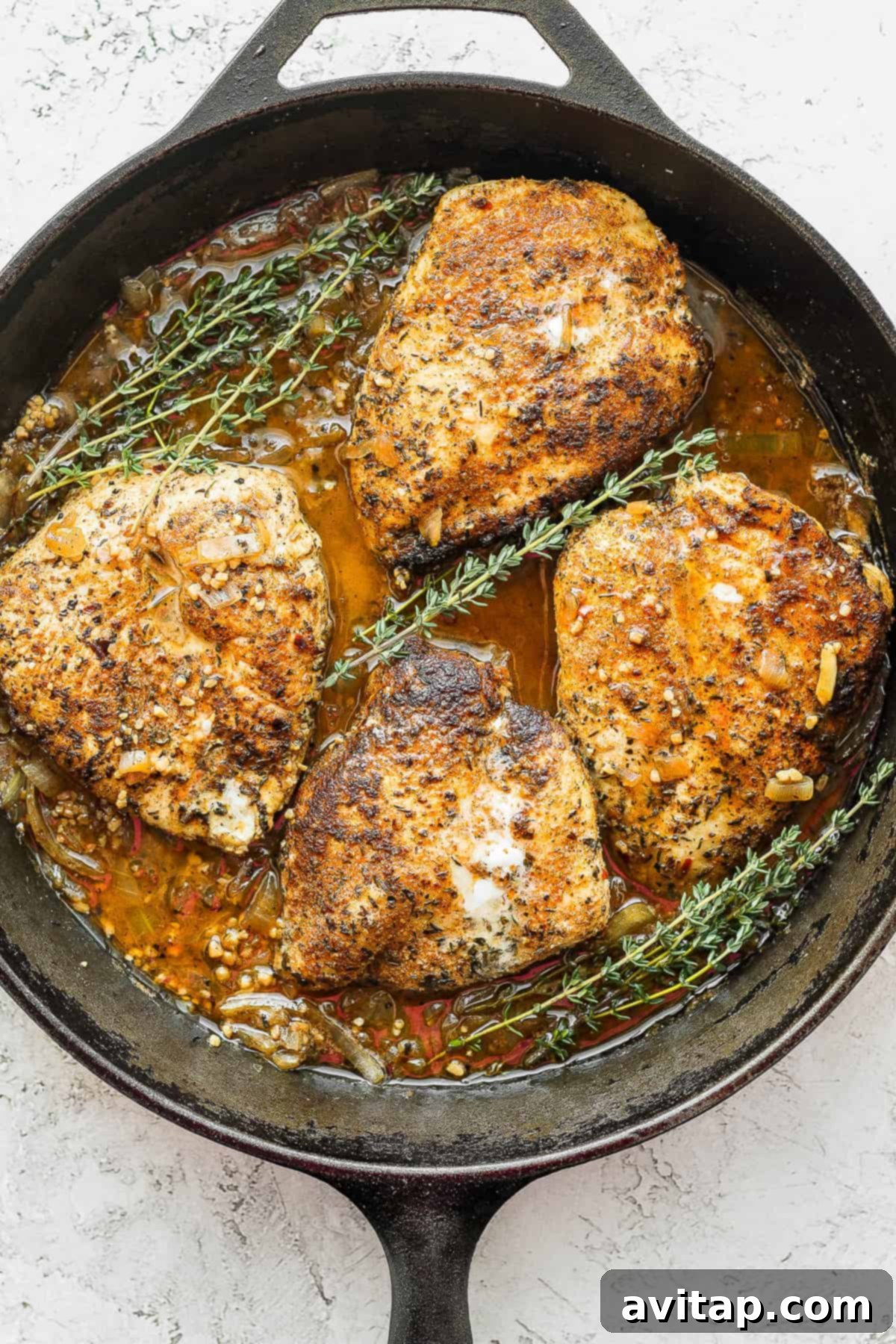 Cooked garlic butter chicken in a cast iron skillet, garnished with fresh thyme sprigs.