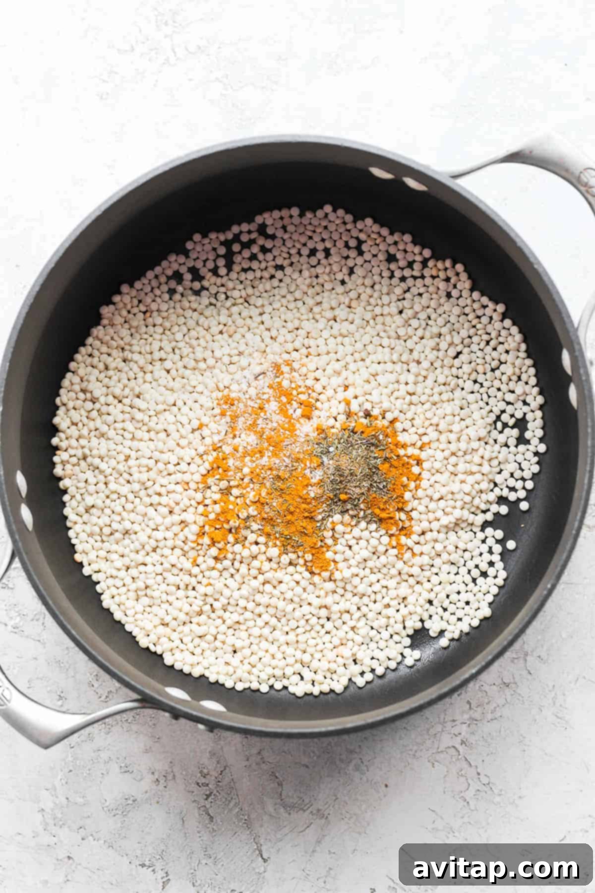 Israeli couscous being toasted with aromatic spices in a pot, enhancing its nutty flavor before cooking.