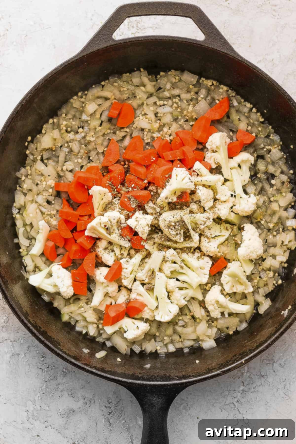 Fresh carrots and cauliflower being sautéed in a cast iron skillet, adding color and nutrients.
