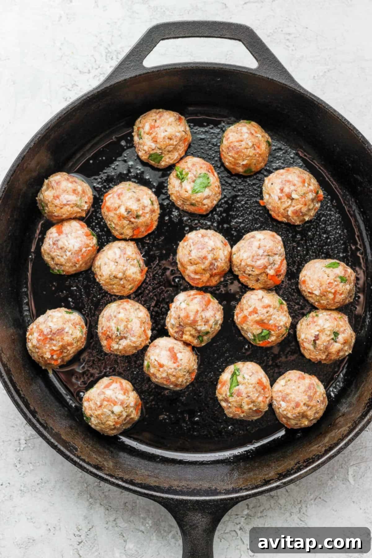 Meatballs browning to a golden crisp in a cast iron skillet, ready to be removed.
