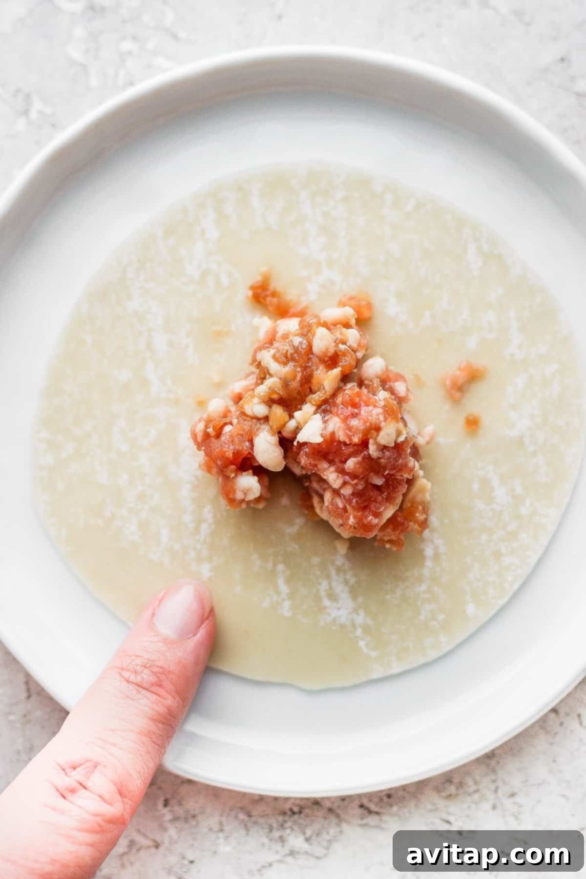 These homemade pork dumplings are packed with savory umami flavors. Make a batch and serve with our amazing sweet dipping sauce that perfectly complements the dumplings. A homemade pork dumpling is carefully placed on a wrapper, ready for folding and sealing